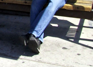 A seated man’s legs and feet, clad in blue denim and black shoes