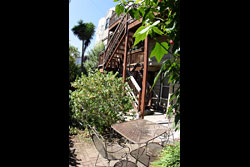 A garden with a wooden staircase coming down from the surrounding building